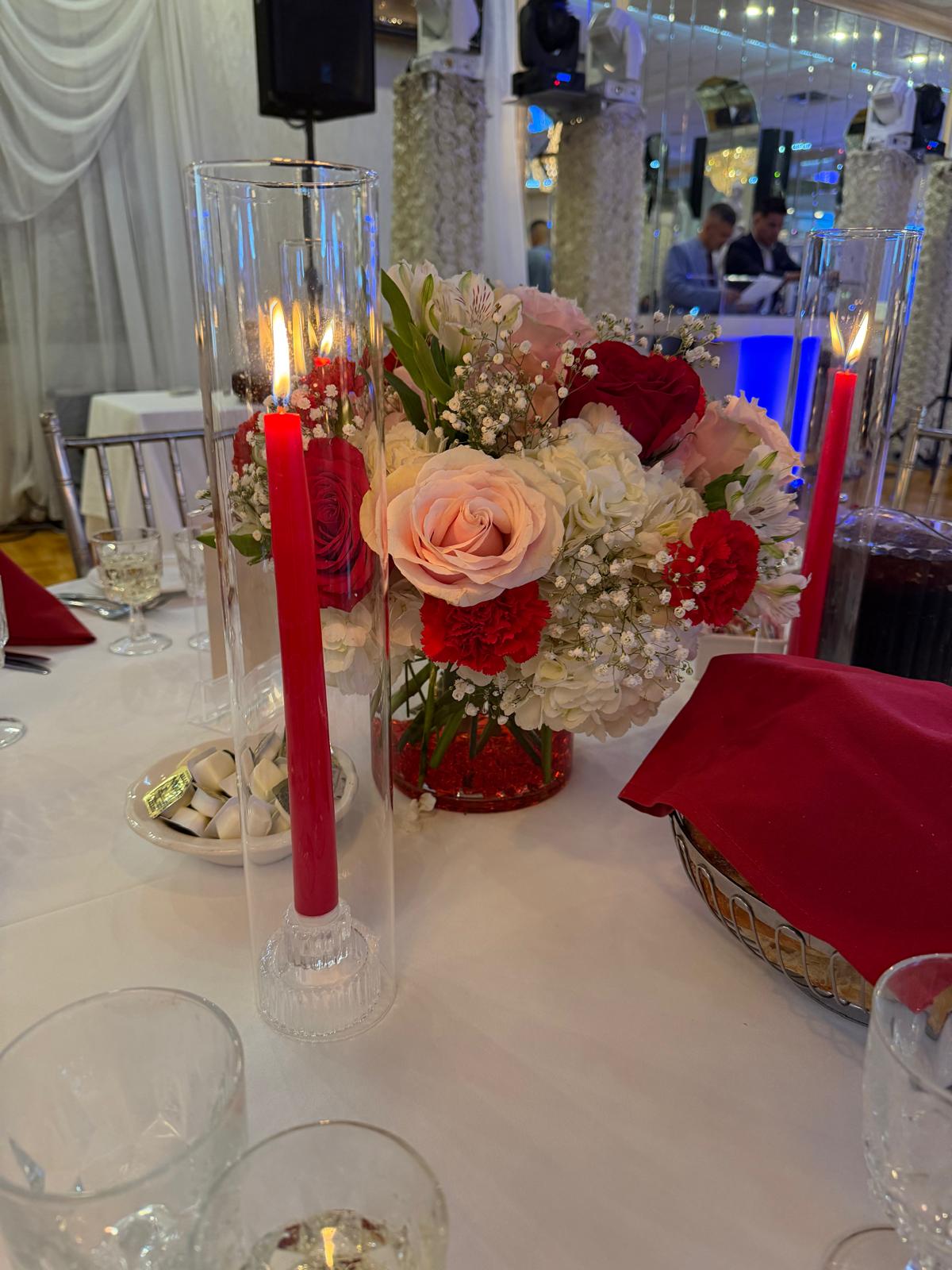 Reception centerpiece of blush and red roses, white hydrangea and carnations between tall red tapers in glass cylinders