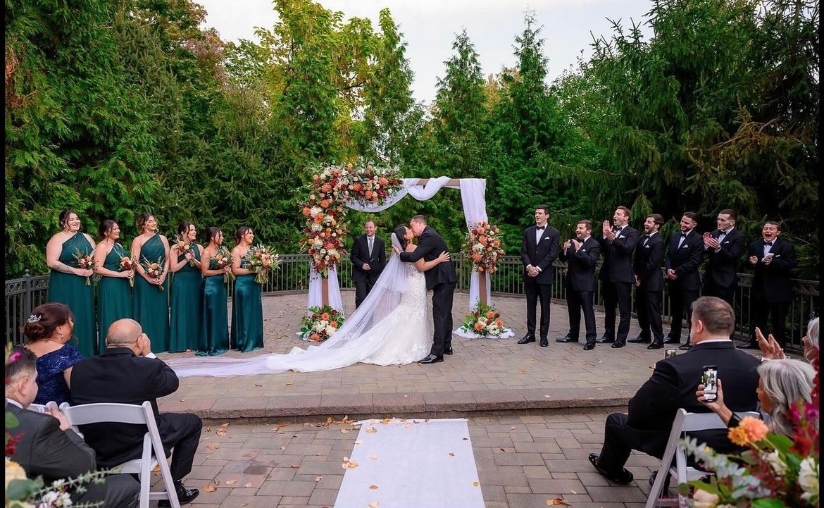 Outdoor terrace ceremony with an autumn floral arch, draped chiffon and the full wedding party