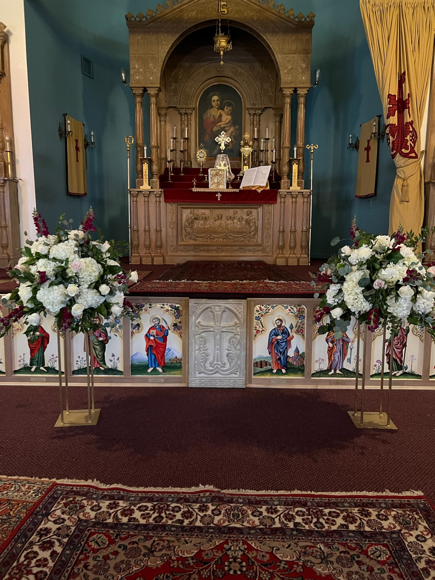 Pair of white hydrangea, rose and burgundy snapdragon arrangements on gold stands framing a church altar