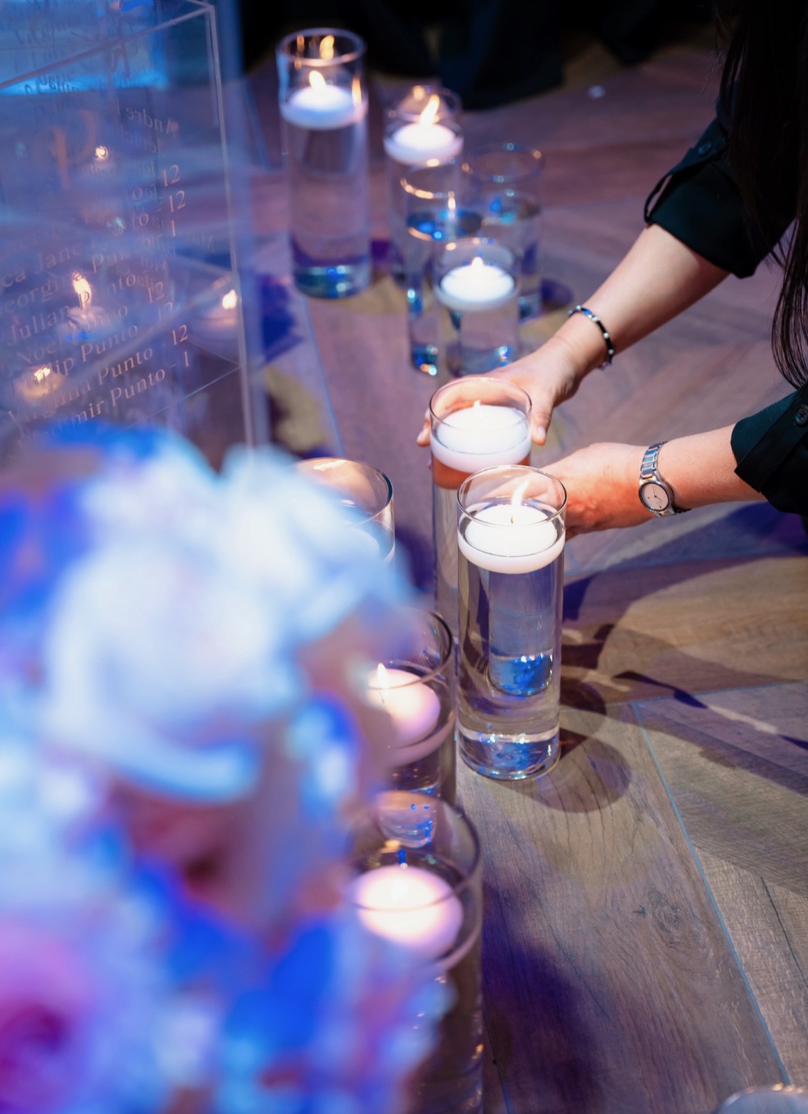 Floating candles in glass cylinders being placed along an acrylic display in blue light