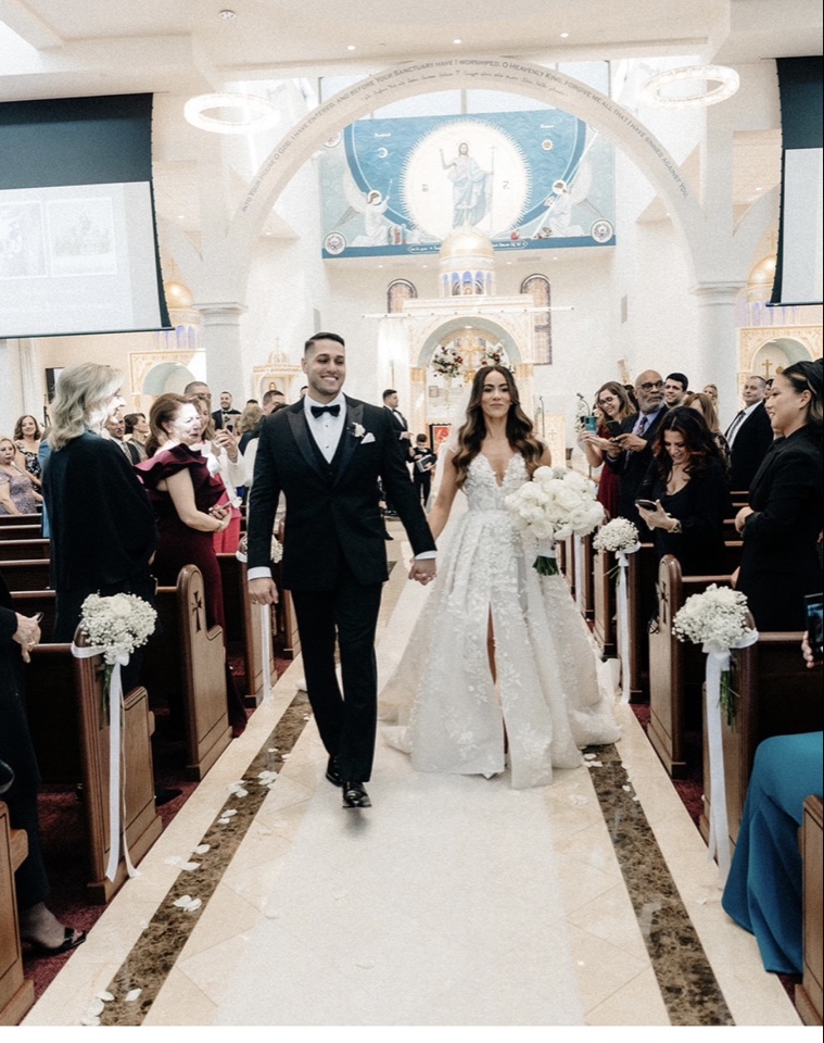 Newlyweds walking back down the church aisle with a white rose bouquet and baby's breath pews