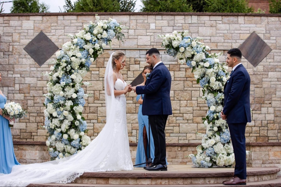 Couple exchanging vows between twin blue and white hydrangea circle arches on a stone terrace