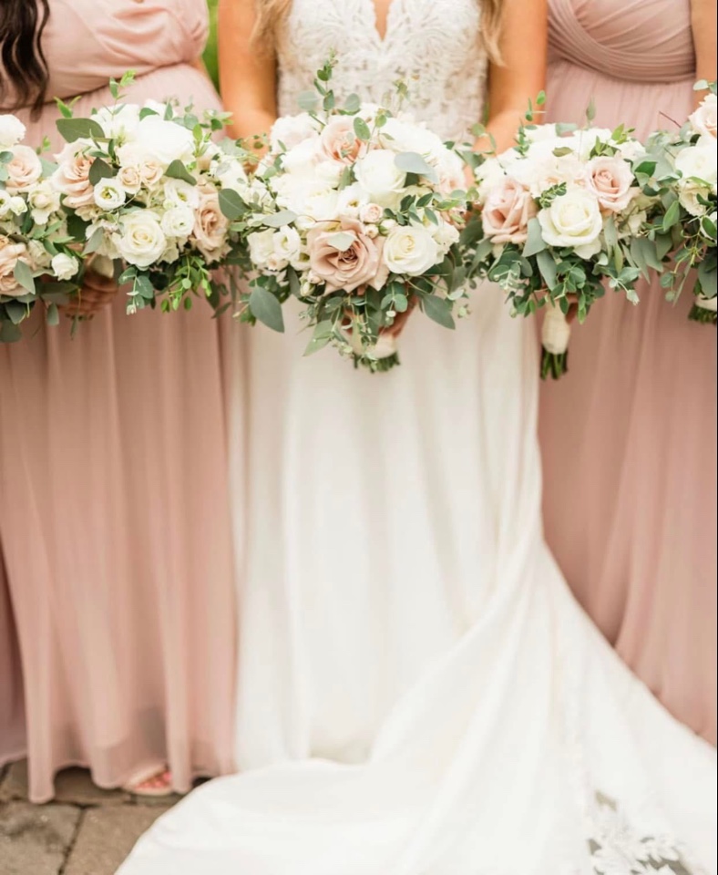 Row of blush and ivory rose bouquets with eucalyptus held over the bride's trailing gown