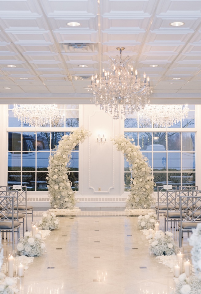 Ballroom ceremony framed by two crescent arches of white baby's breath and candles