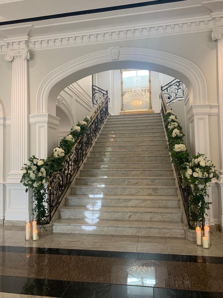 Grand marble staircase dressed with white hydrangea, roses and trailing greenery beside pillar candles
