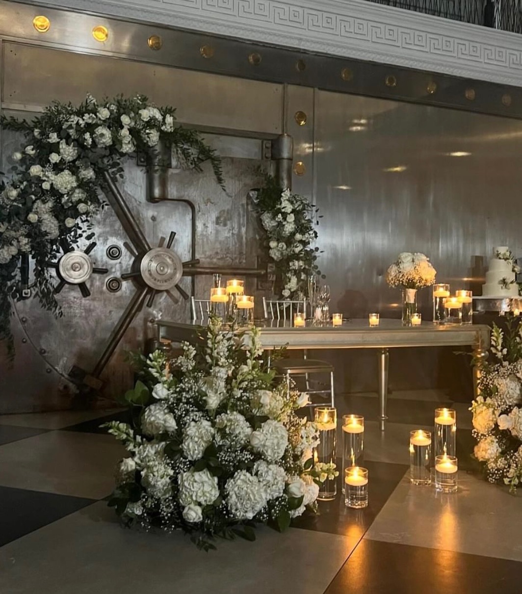 Candlelit sweetheart table against a vintage steel bank vault door dressed with white hydrangea and greenery