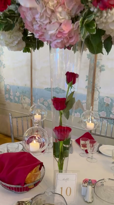Video still of a tall red and blush rose centerpiece with glass candle hurricanes