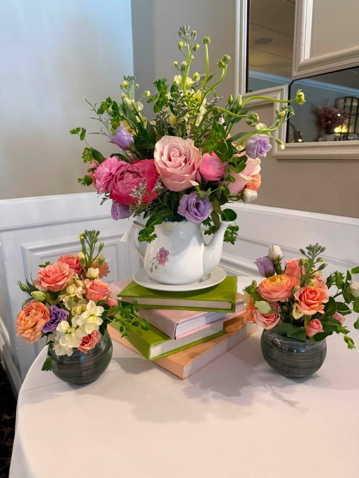 Vintage teapot overflowing with peach, pink and lavender blooms atop a stack of pastel books with matching posies