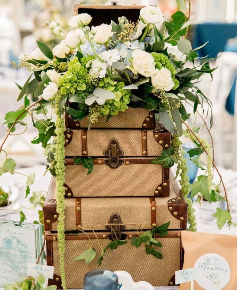 Stack of vintage suitcases crowned with white roses, green hydrangea and trailing ivy
