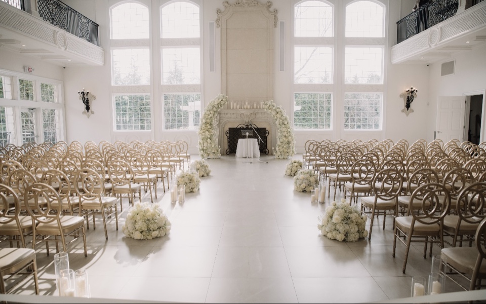 Ballroom ceremony with a white hydrangea arch at the fireplace and gold chiavari chairs