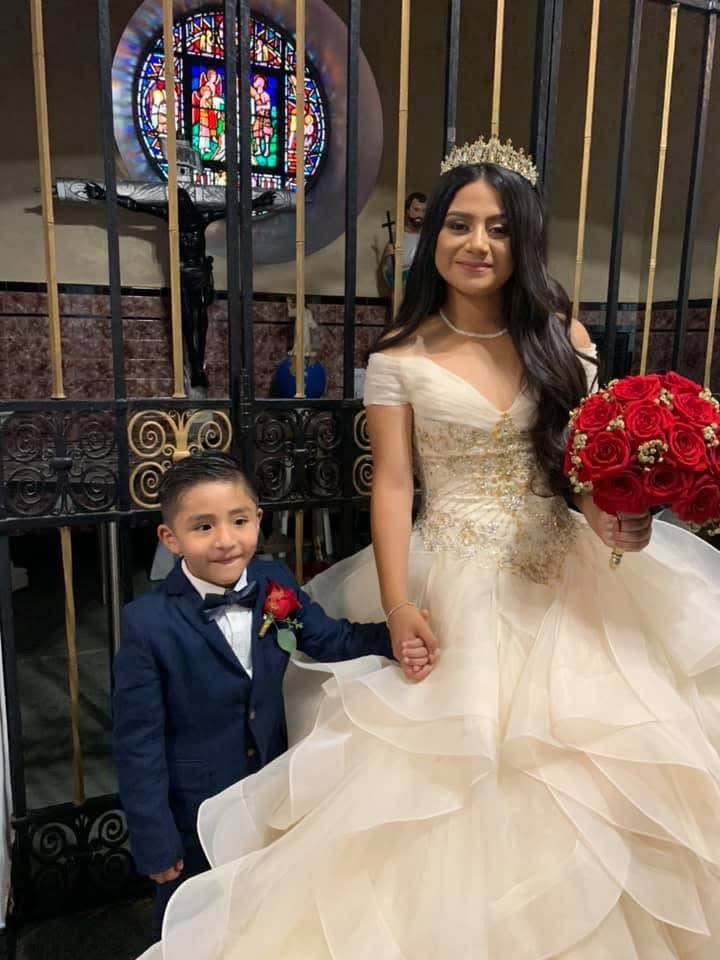 Quinceañera in a gold-embroidered ivory gown with her young escort, holding a red rose bouquet at the church