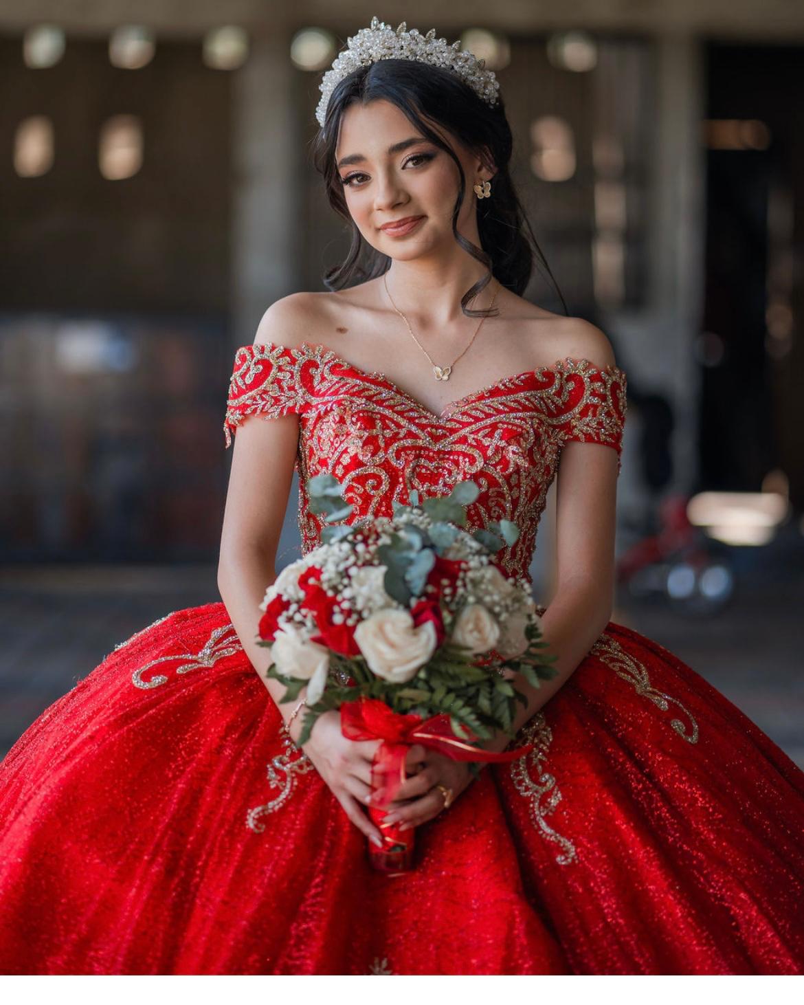 Quinceañera in an embroidered red gown and tiara holding a red and ivory rose bouquet with eucalyptus