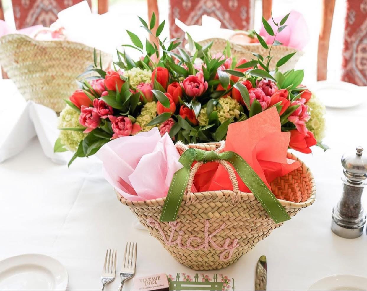 Vivid coral and pink tulip centerpiece behind a straw guest tote embroidered Vicky with pink tissue