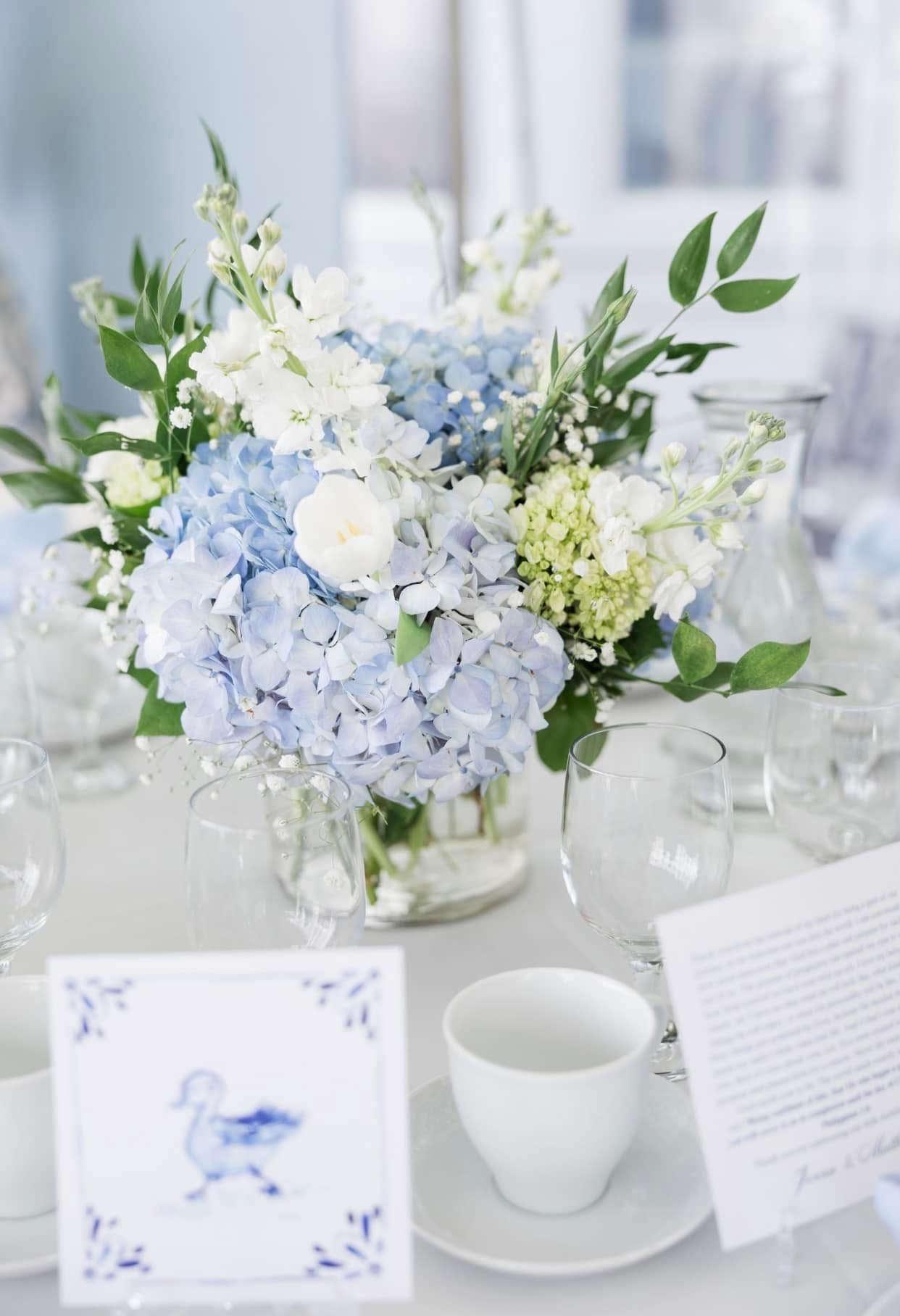 Baby shower centerpiece of blue hydrangea, white stock and viburnum on a bright table