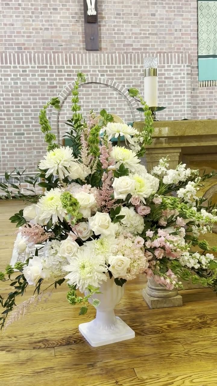 Video still of a white urn arrangement of roses, dahlias and blush snapdragons at a church altar