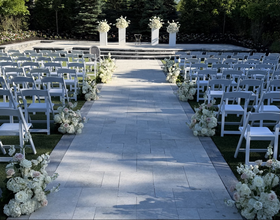 Garden ceremony aisle lined with white and blush arrangements leading to tall white pedestals