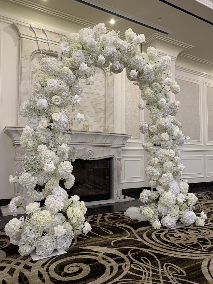 Tall arch of white hydrangea and roses framing a marble fireplace in a ballroom ceremony