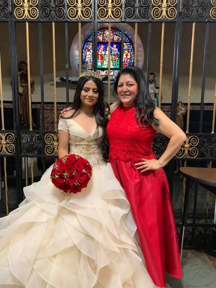 Birthday girl in a gold and white gown holding a hand-tied red rose bouquet with her mother
