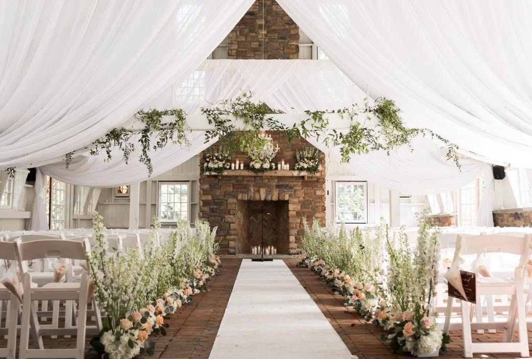 White-draped pavilion ceremony with delphinium and blush aisle arrangements leading to a stone fireplace