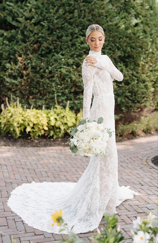 Bride in a long-sleeve lace gown holding a white bouquet with eucalyptus in the garden