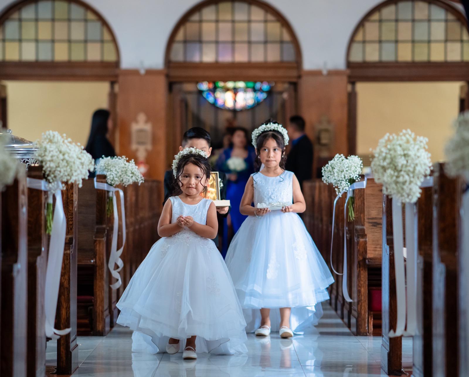 Flower girls walking the church aisle carrying white posies with baby's breath pew bundles