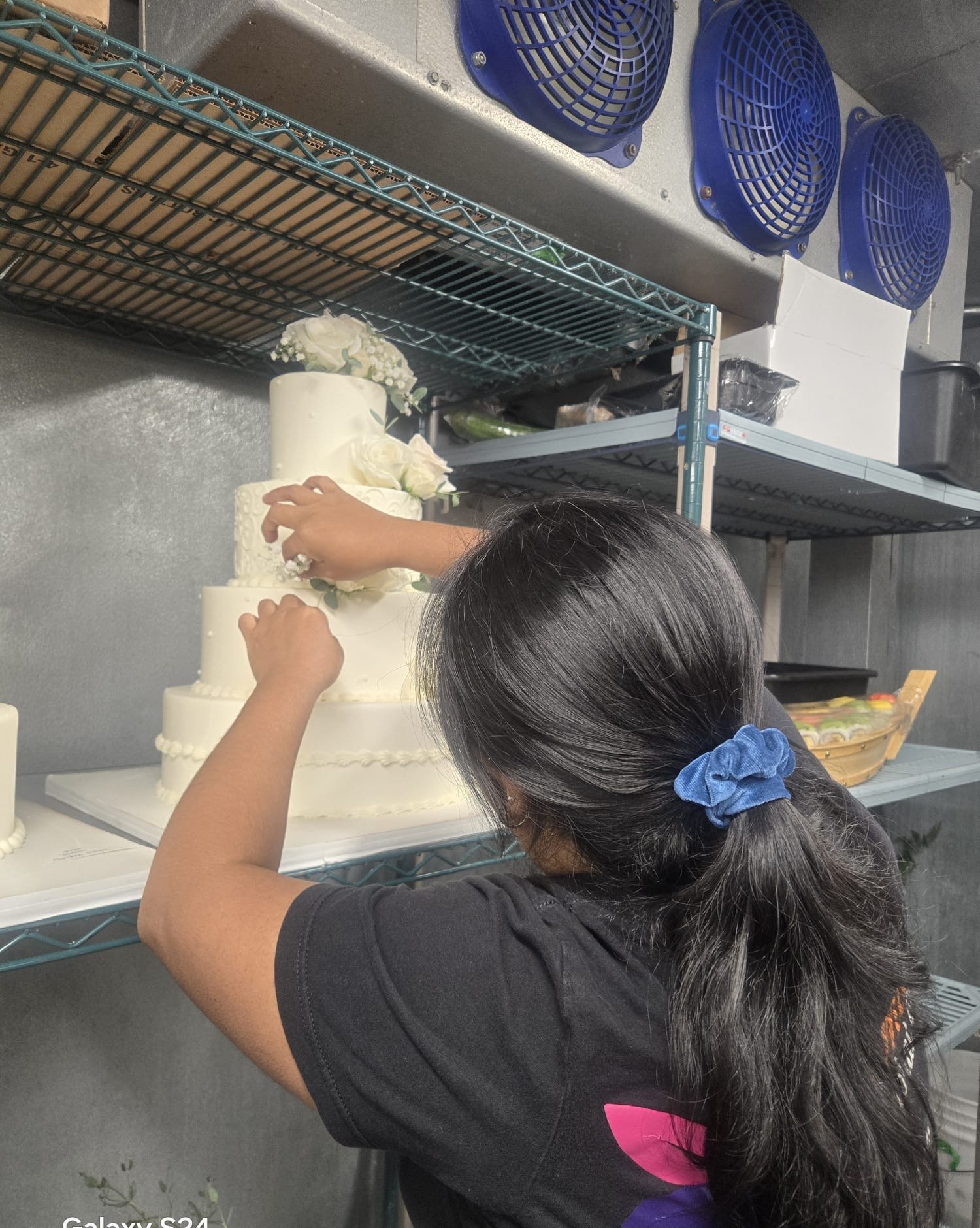 A Yumila’s florist finishing a tiered wedding cake with fresh white roses and eucalyptus