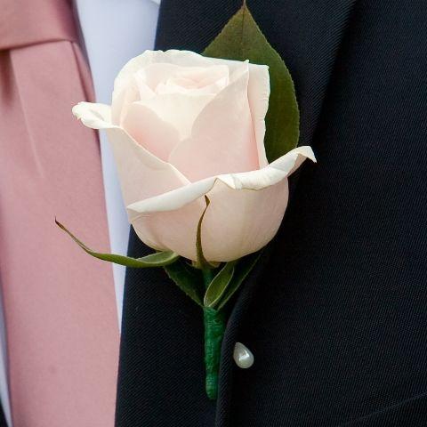 Blush rose boutonniere with a green leaf on a black suit with a dusty pink tie