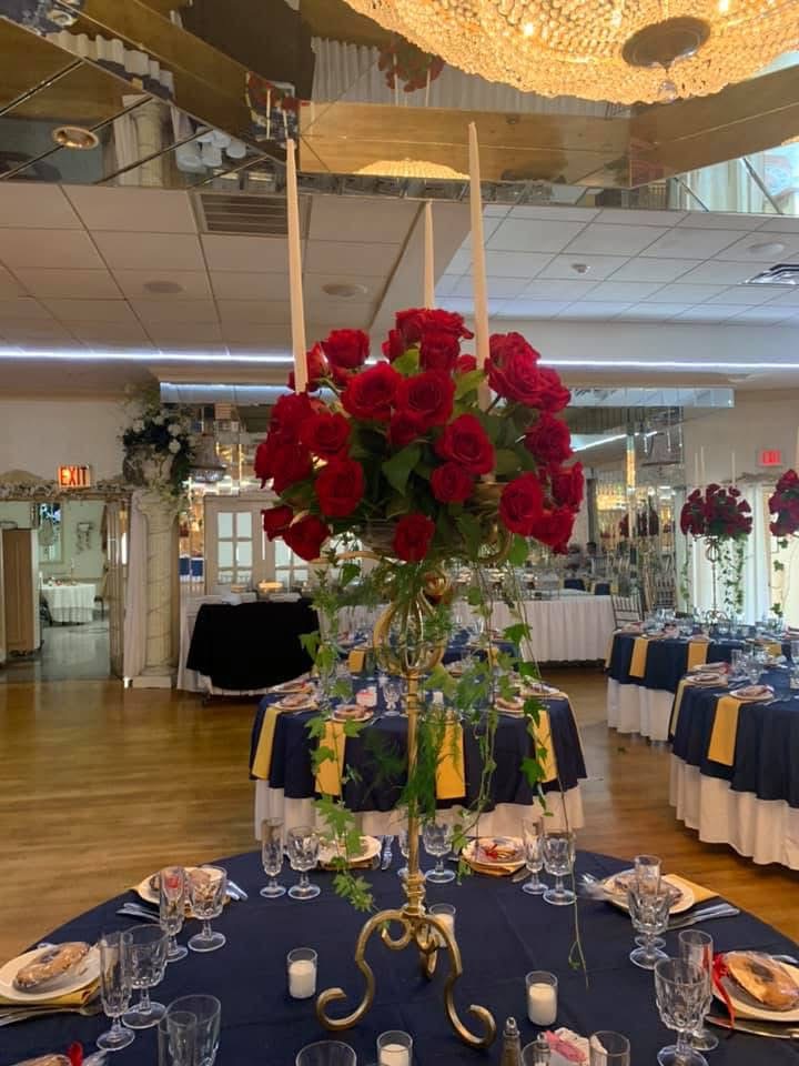 Tall gold candelabra crowned with red roses and trailing ivy above navy and gold reception tables