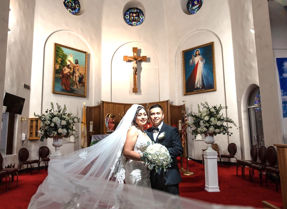 Couple at the church altar flanked by tall white and green arrangements on pedestals