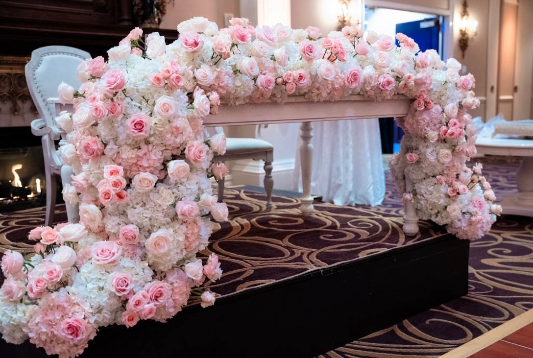 Sweetheart table wrapped in a solid frame of pink and white roses and hydrangea beside a fireplace