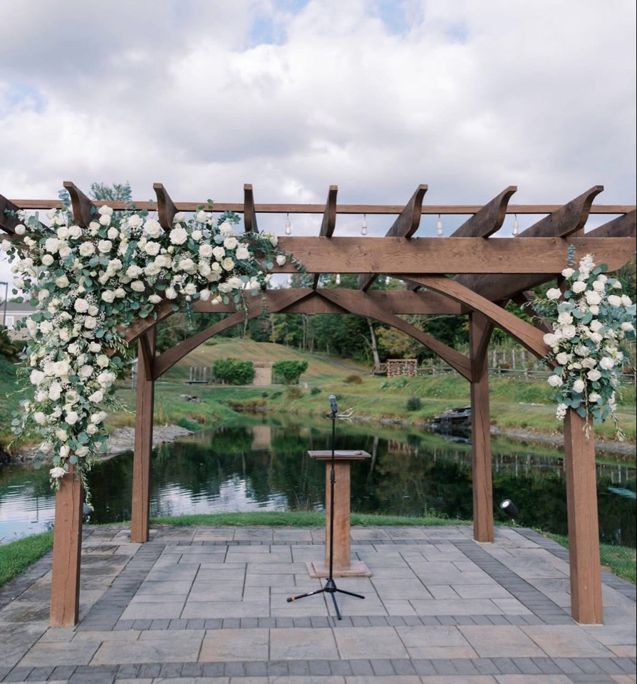 Wooden lakeside pergola draped with white roses and eucalyptus