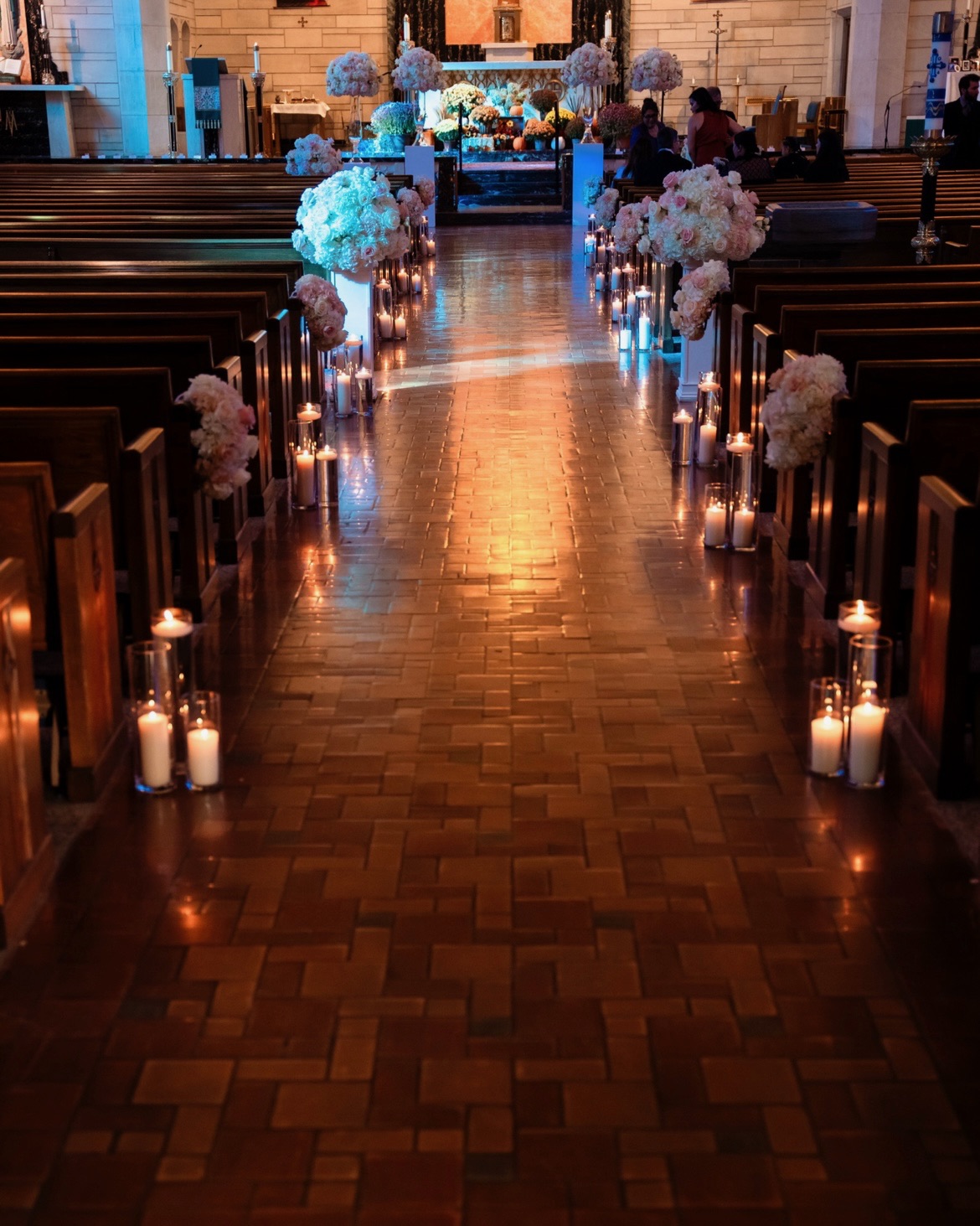 Full church aisle in candlelight with blush pew florals and tall altar arrangements