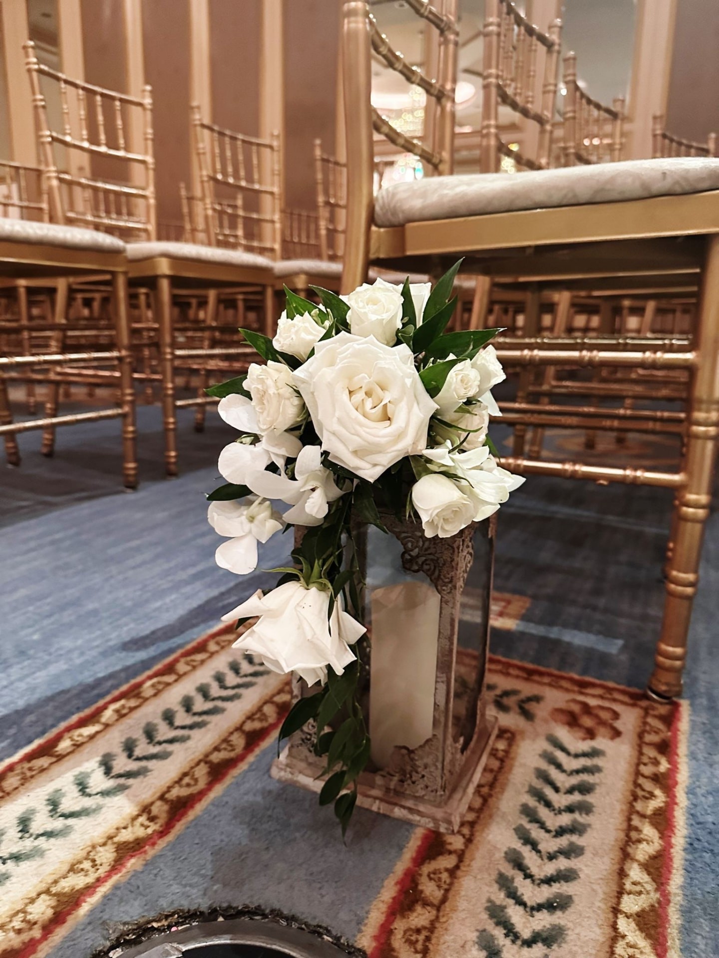 Cascading white roses and orchids on an aisle lantern between gold chiavari chairs