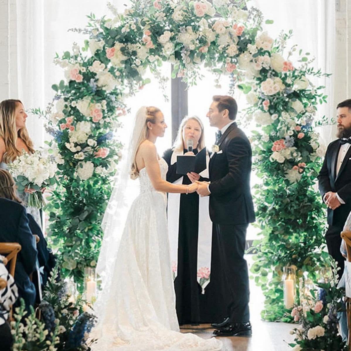 Couple exchanging vows beneath a circular arch of garden roses, hydrangea and eucalyptus