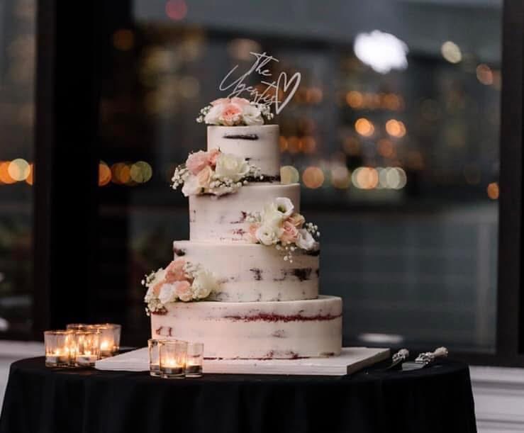 Four-tier naked cake with blush and ivory roses surrounded by candles at night