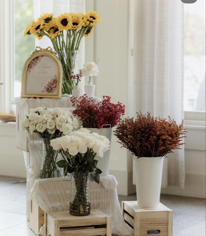 Bloom bar display of white roses, burgundy blooms and sunflowers in buckets on wooden crates